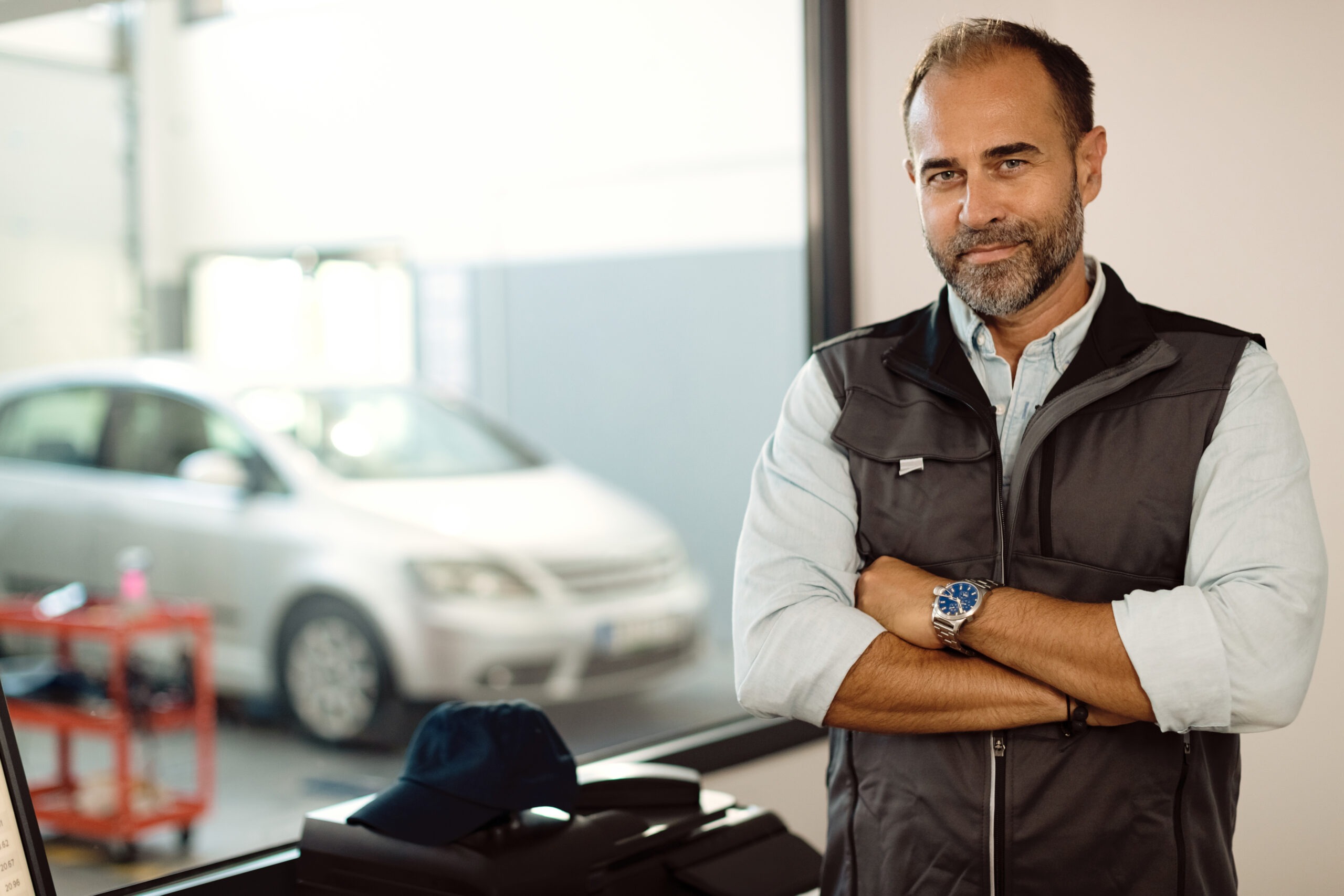 Portrait of confident auto mechanic standing with crossed arms in the office at his repair shop.
